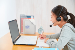 Asian woman wearing a headset, focused on her laptop while working in a modern office environment.