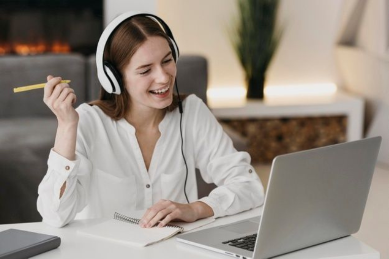 A woman with headphones sits at a desk, focused on her laptop, engaged in work or study.